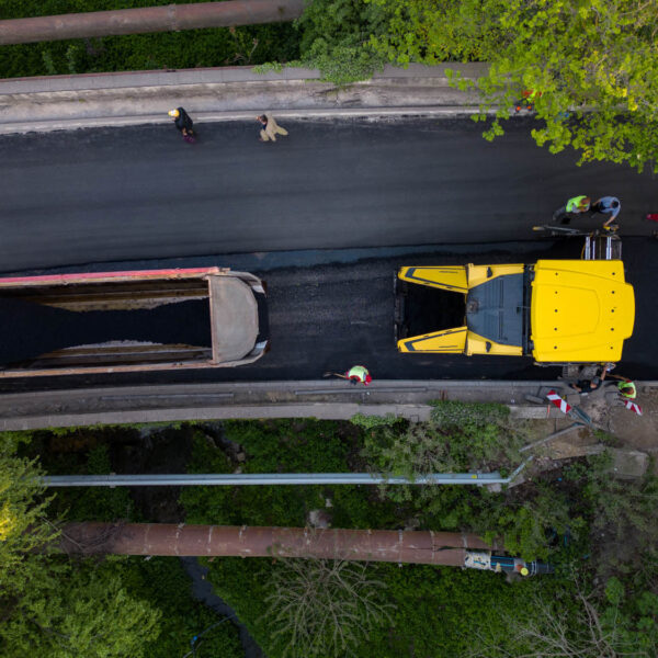 Aerial view of the construction of a new road as asphalt pavers, rollers, machinery, and workers come together to build a vital transportation link. Witness the impressive coordination and teamwork from above.