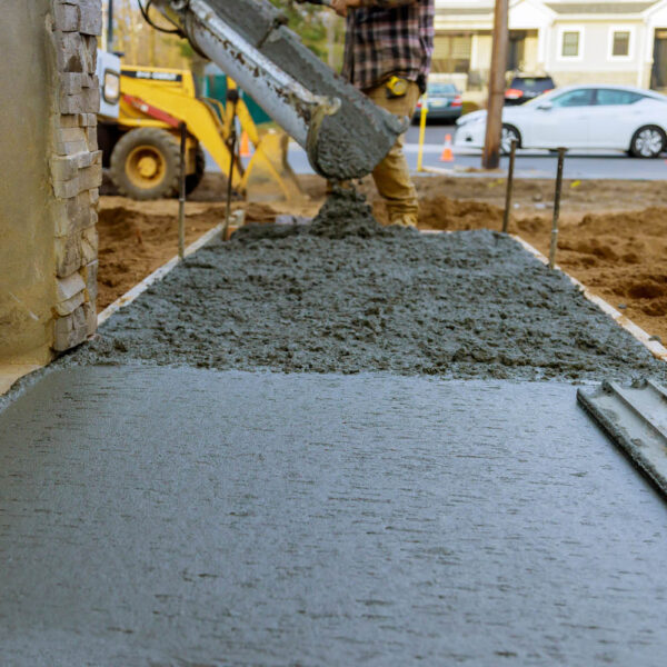 Construction worker pouring reinforced concrete cement for sidewalk in new residential home